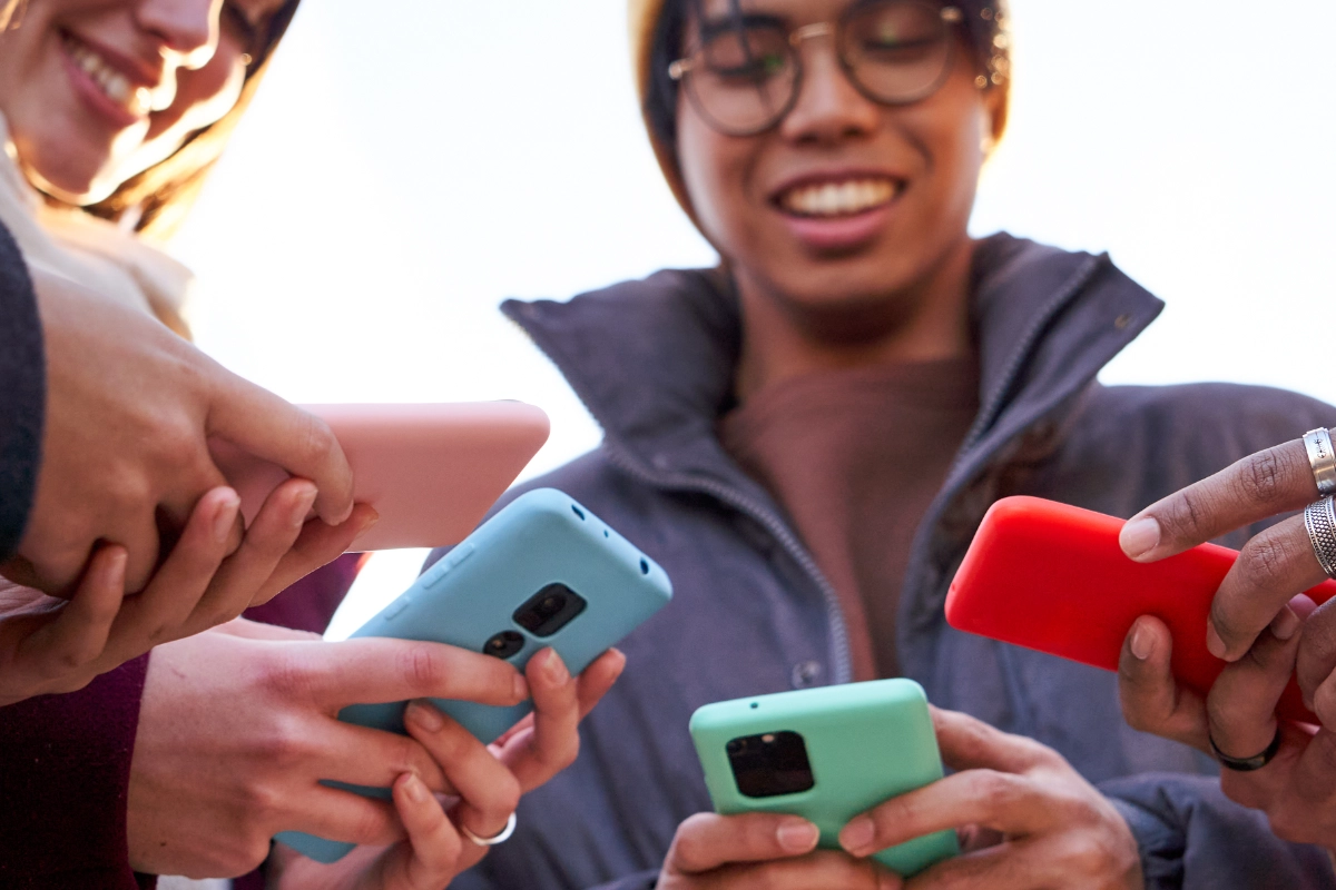 friends standing in circle using phone outdoors.